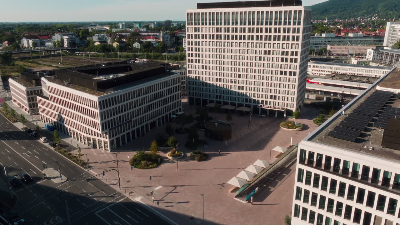 Modern commercial center (likely Bahnstadt). Features large office buildings, public plaza, railway infrastructure, and the forested hills defining the urban edge. Highlights business and transit