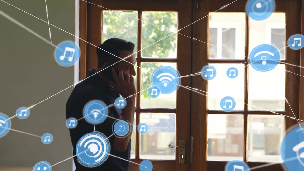 Network of digital icons against caucasian man talking on smartphone near the window at home
