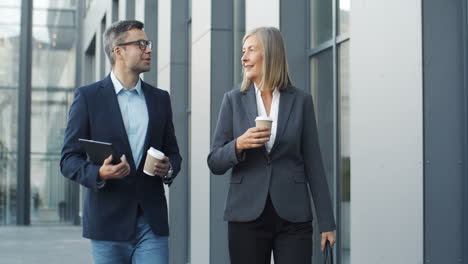 cuc businessman and businesswoman walking the street together with coffee to go in hands and talking cheerfully