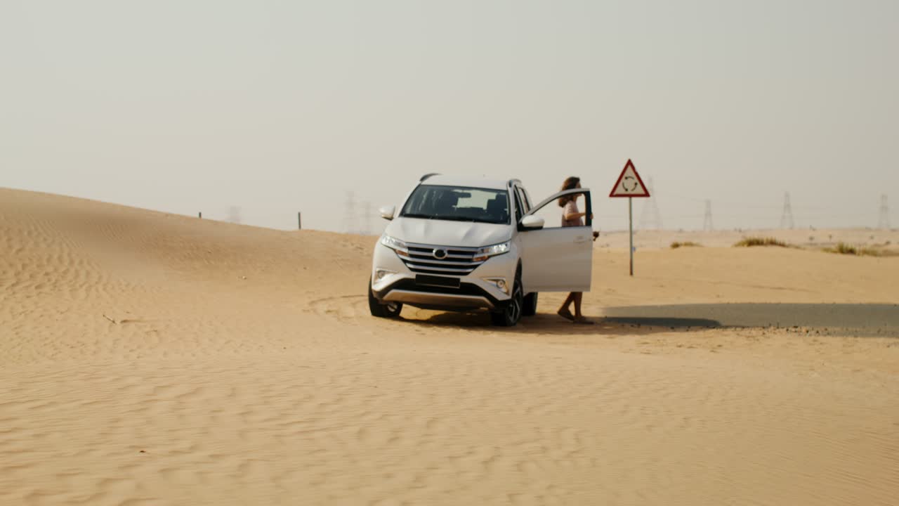 mujer de pie junto a un coche en el desierto