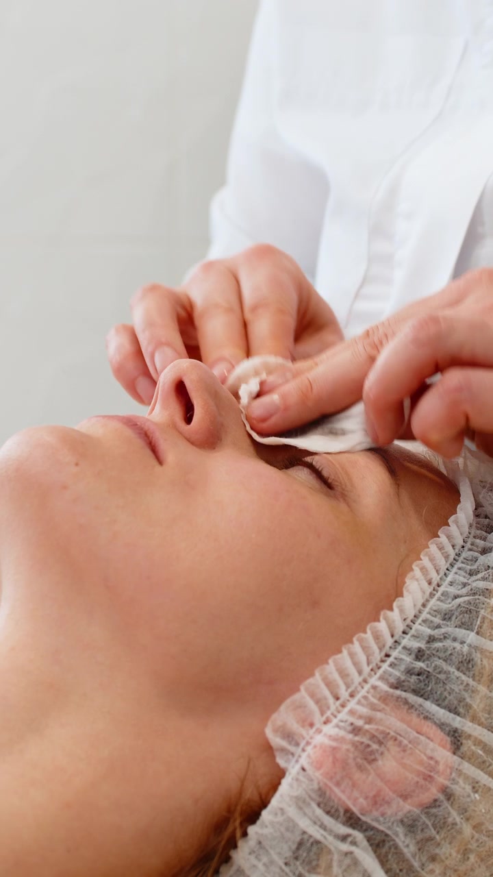 Kosmetikerin reinigt das Gesicht einer Frau mit Wattepad vor einer Peeling-Behandlung in Schönheitsklinik, Salon oder Spa