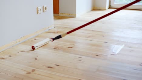 roller applies glossy protective finish on sanded wooden floor in bright indoor room