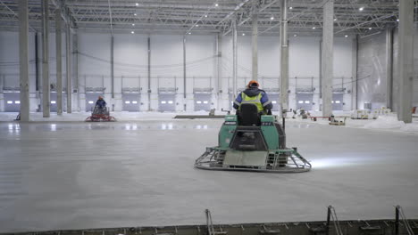 workers using power trowels to finish a concrete floor in a warehouse