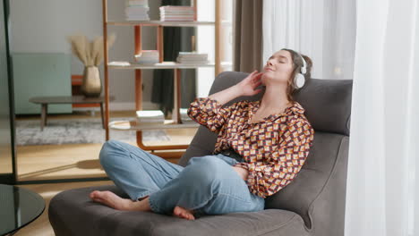 young woman with headphones relaxes in living room with eyes shut, pan