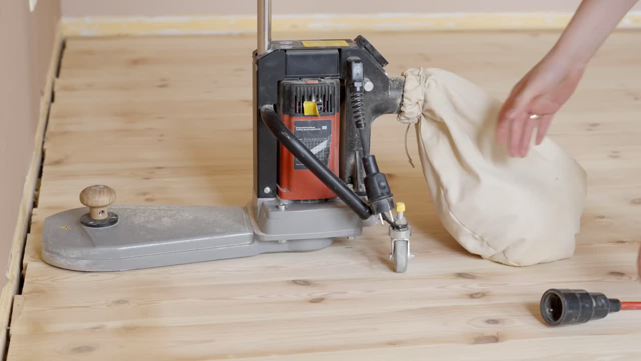 Professional prepares electric sander for refinishing wooden floor edges safely