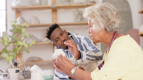 Two-happy-diverse-male-and-female-potters-holding-pots-and-discussing-in-pottery-studio,-slow-motion