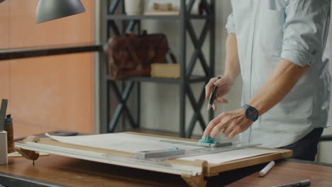 architect man sits at drafting table in modern industrial office during the day. architect working on blueprint with spesial tools and pencil close up. male architect at work only hands with ruler and pencil. design of the house. engineer. tools for drawing. creating a drawing.