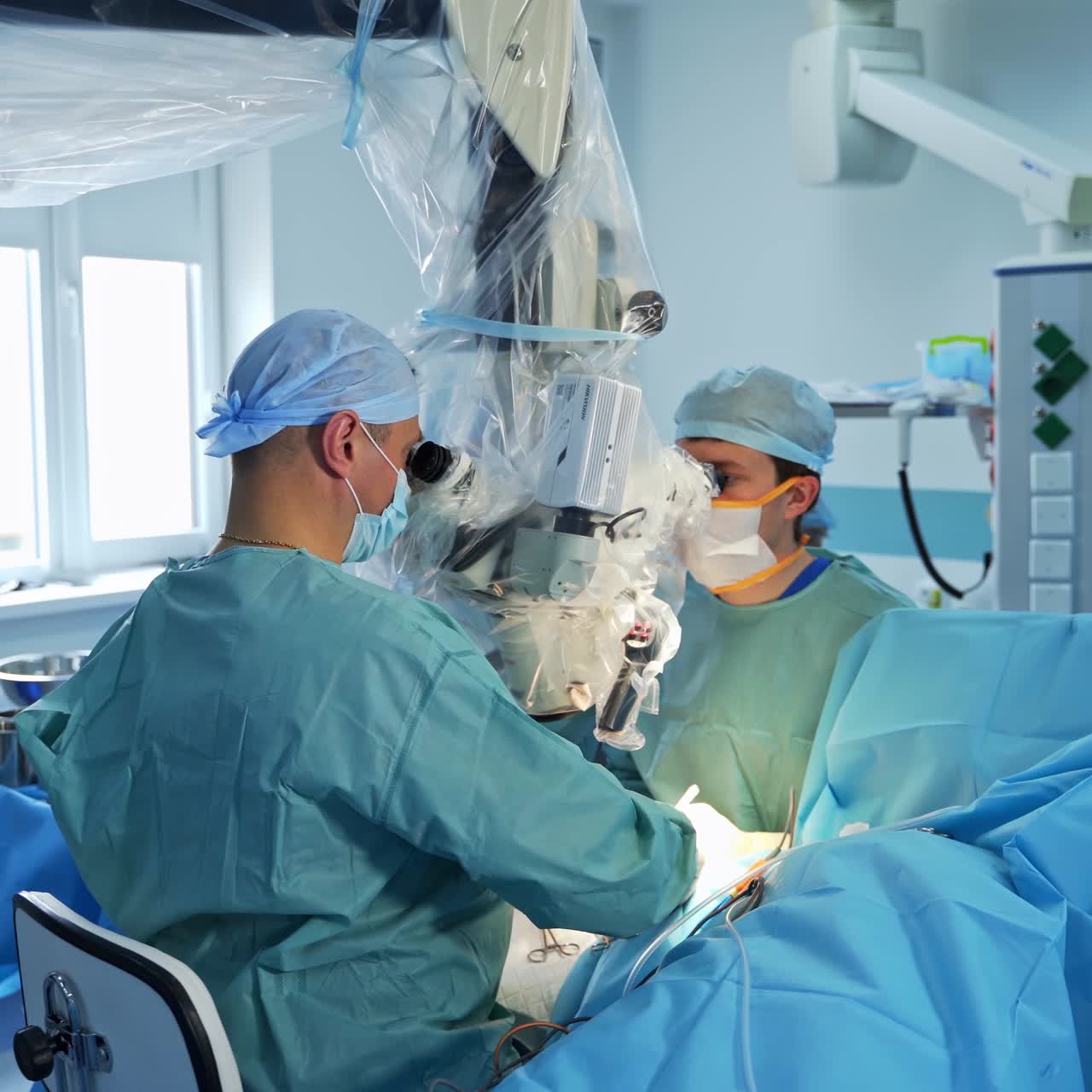 Two surgeons look into binoculars sitting over the patient. Team of experienced doctors conducting surgery