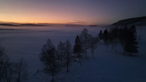 snowy landscape at dusk with fog over the fields and a colorful sky near sundsvall, sweden, aerial view