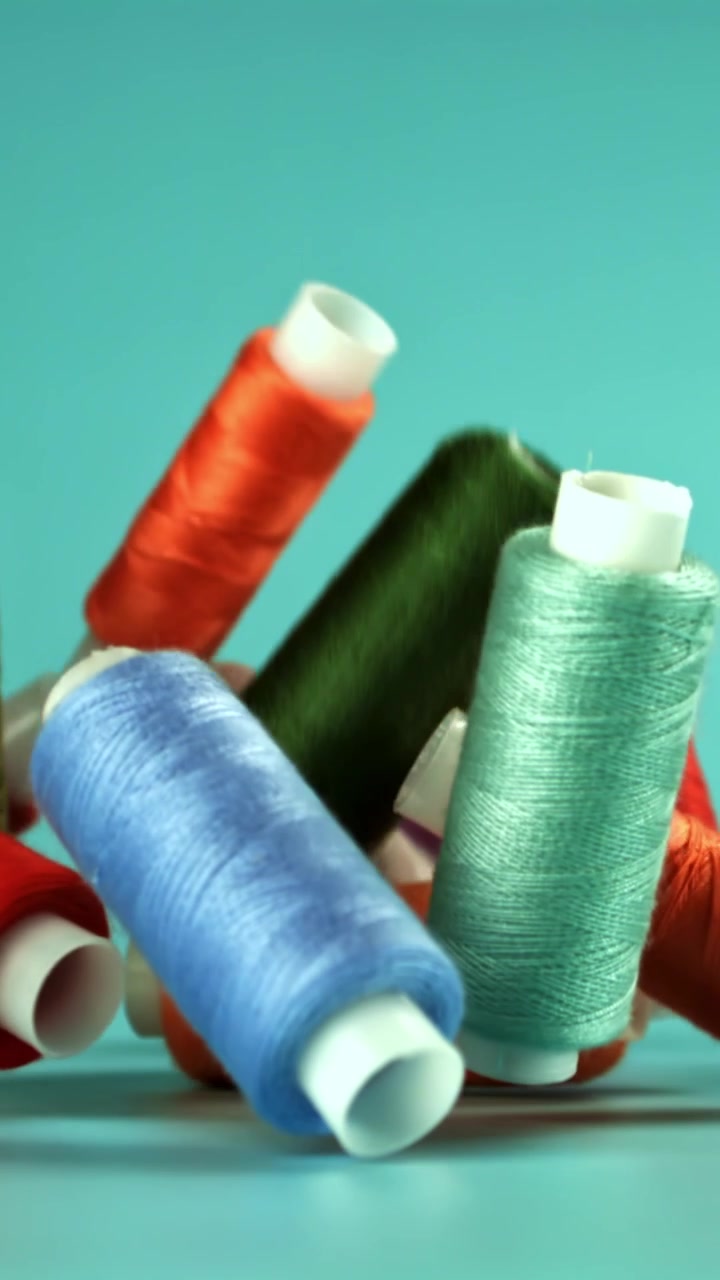 Colorful Spools of Thread Falling in Slow Motion onto a Turquoise Background
