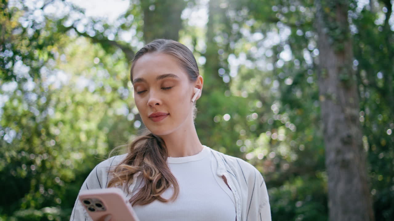 una mujer romántica usando una aplicación de teléfono inteligente escuchando música en un paseo por el bosque de cerca.