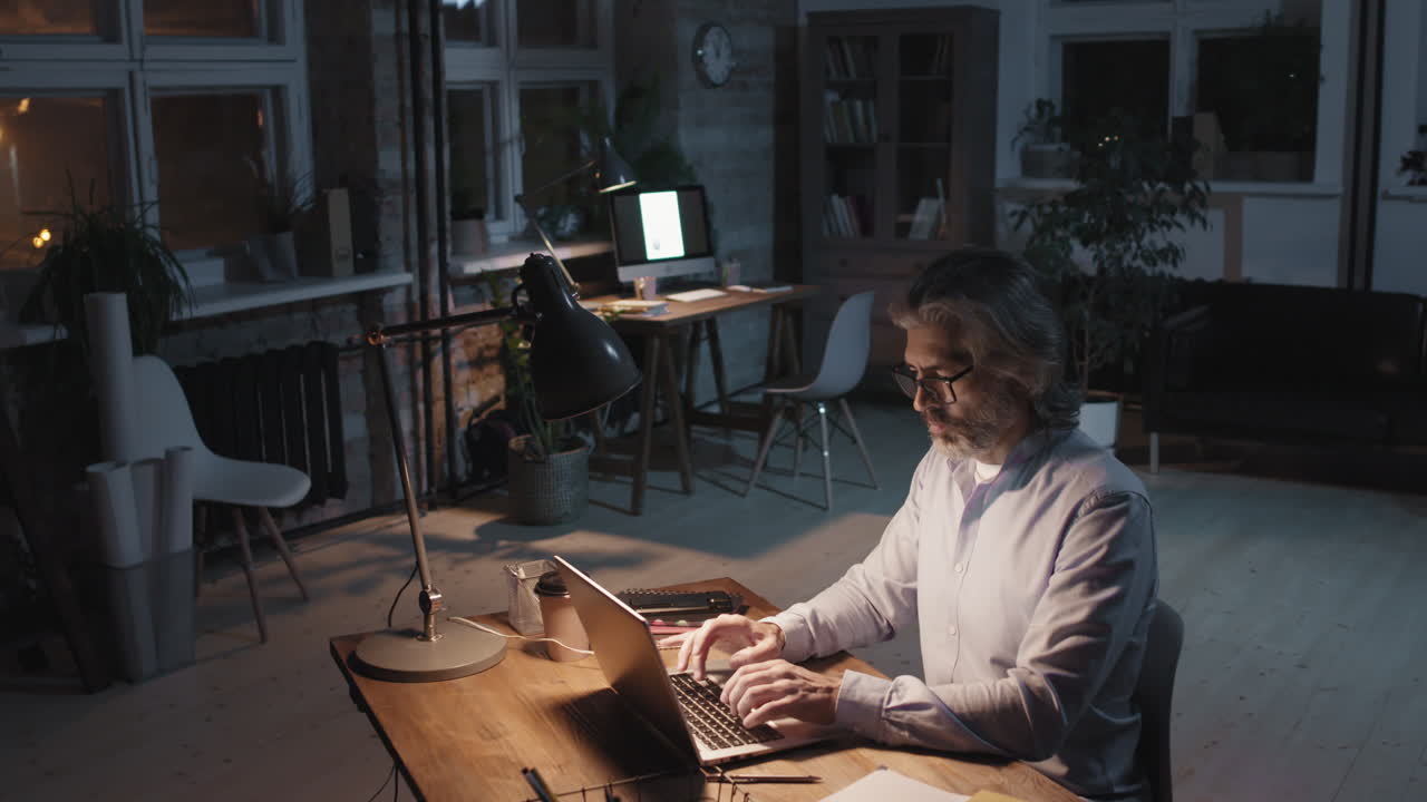 Man working on laptop at desk in dimly lit office at night