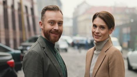 caucasian good looking stylish man and woman standing in the street in autumn, then they turn their faces to the camera and smile cheerfully