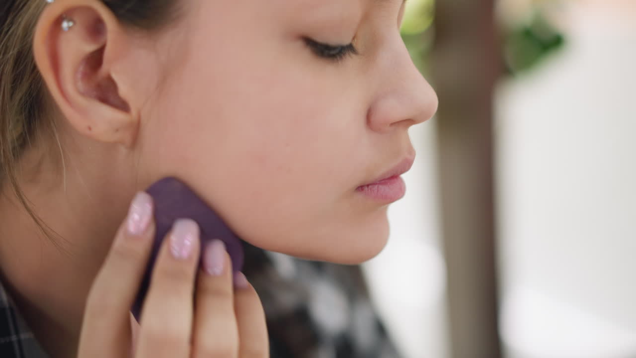 primer plano de una mujer aplicando maquillaje a lo largo de la mandíbula usando esponja de belleza, centrarse en la mezcla uniforme de la fundación para un aspecto impecable, iluminación suave y fondo borroso mejoran la rutina de belleza énfasis