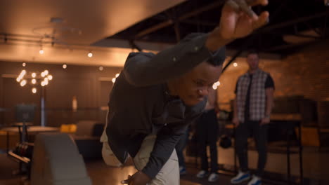 Portrait-of-an-African-American-man-throws-a-bowling-ball-and-knocks-out-a-shot-with-one-shot.-Multi-ethnic-group-of-friends-bowling
