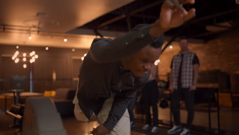 portrait of an african-american man throws a bowling ball and knocks out a shot with one shot. multi-ethnic group of friends bowling