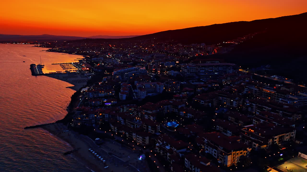 Sunset view of a coastal town at night. Warm colors paint the sky as the coastal town transitions to evening, lights twinkling along the waterfront