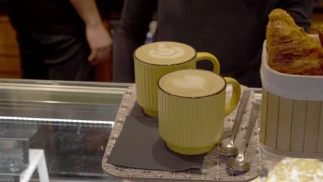 coffee cups with milk designs sit next to croissants on the coffee shop counter