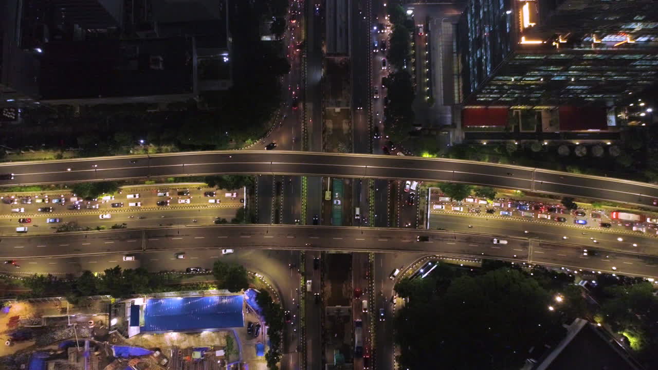 자카르타 쿠닌간 지구, 쿠닝안 지역의 번잡한 교차로의 빌딩 탑 샷과 그 사이에서 야간 비행은 교통량이 많은 도시 벌목을 만듭니다.