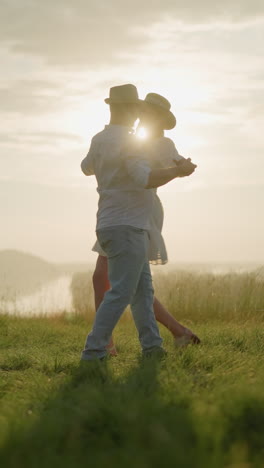 dos parejas bailan felices en una colina cubierta de hierba iluminada por el sol al lado de un lago pacífico. el hombre, vestido con una camisa blanca, sombrero y vaqueros, comparte un momento con su esposa, que lleva un vestido blanco y un sombrero negro