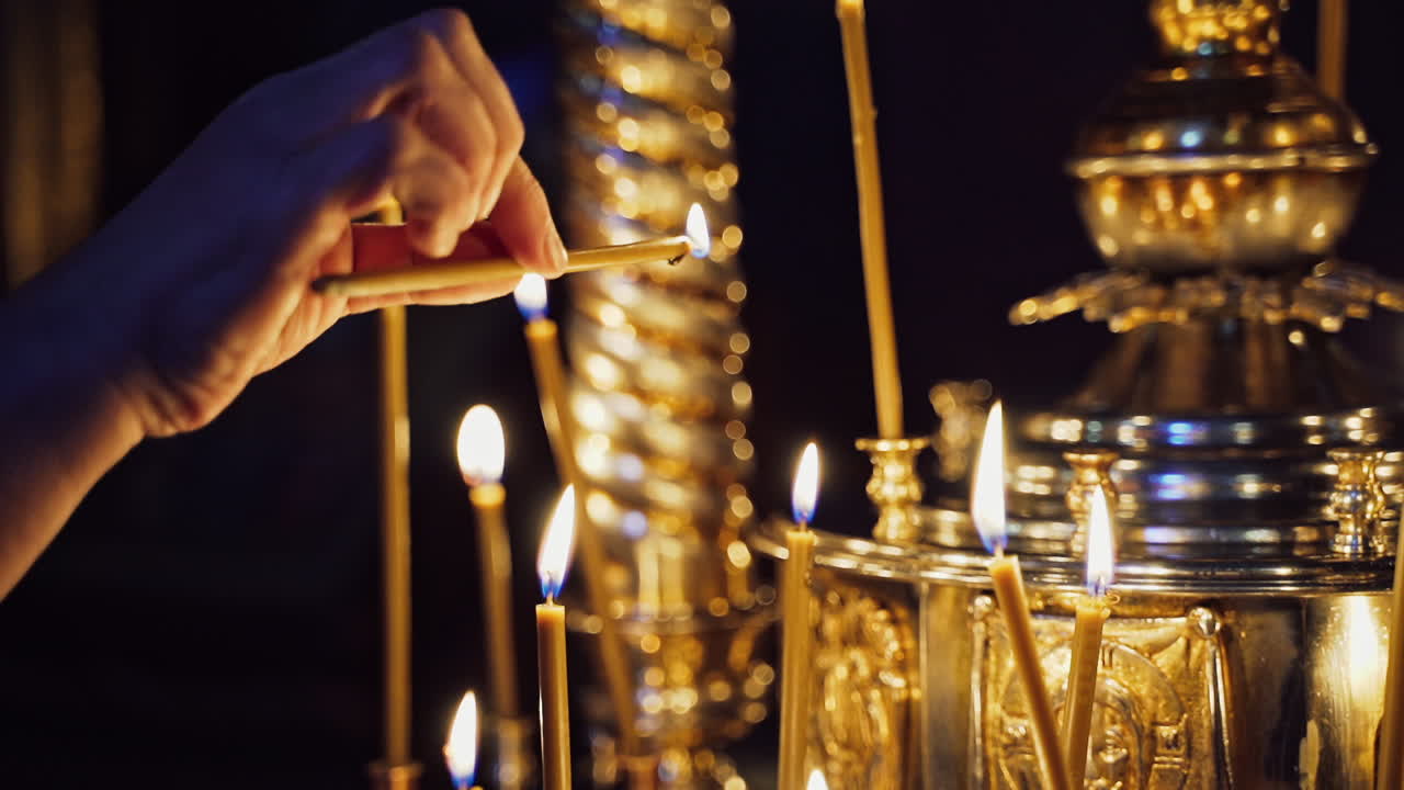 Woman's hand lighting a candle and putting it among other candles in a church. Candles are lit for prayer intentions.