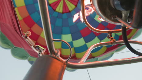 close up of hot air balloon burner blasting intense flame into colorful canopy during inflation or ascent showing metal pipes, fire blast, and vibrant fabric segments under clear sky