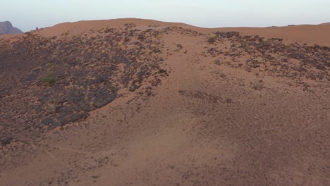 Drone-flying-over-mountain-revealing-car-driving-through-desert,-Zagora-in-Morocco