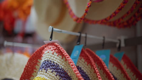 close-up of a hand delicately removing a colorful woven hat from a rack in a retail store, the hat features vibrant patterns with orange, yellow, and purple accents