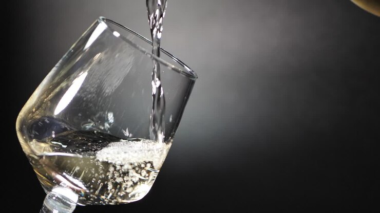 Una donna versa un bicchiere di vino su sfondo nero, primo piano.