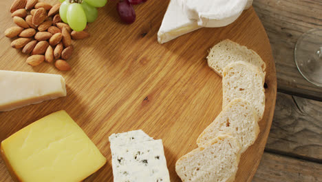 video of cheeses, bread, nuts and grapes on board, with wine glass on wooden table