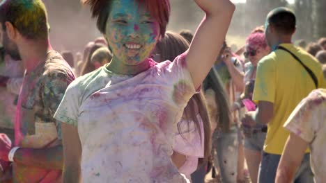 two young multi-ethnic girlfriends are jumping and dancing in crowd on holi festival in daytime in summer, friendship concept, holiday concept