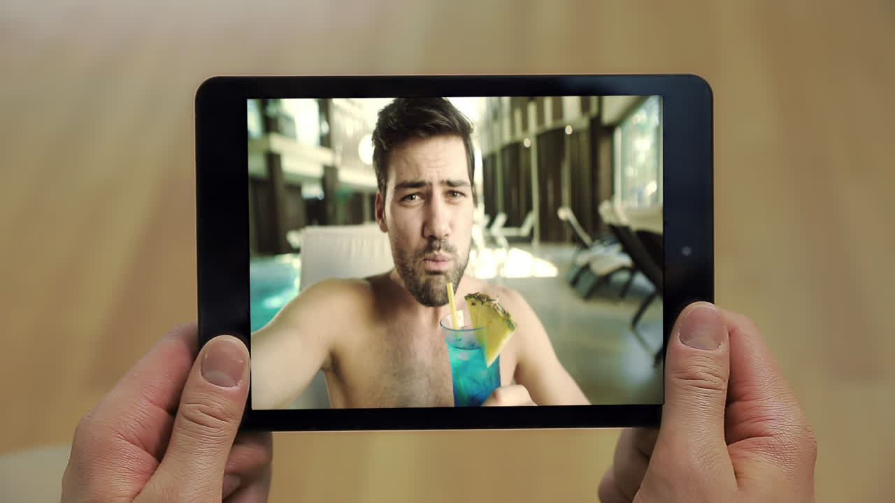 Uomo rilassato che effettua una videochiamata con un tablet inquadrato da vicino a bordo piscina. Ragazzo che tiene in mano un tablet