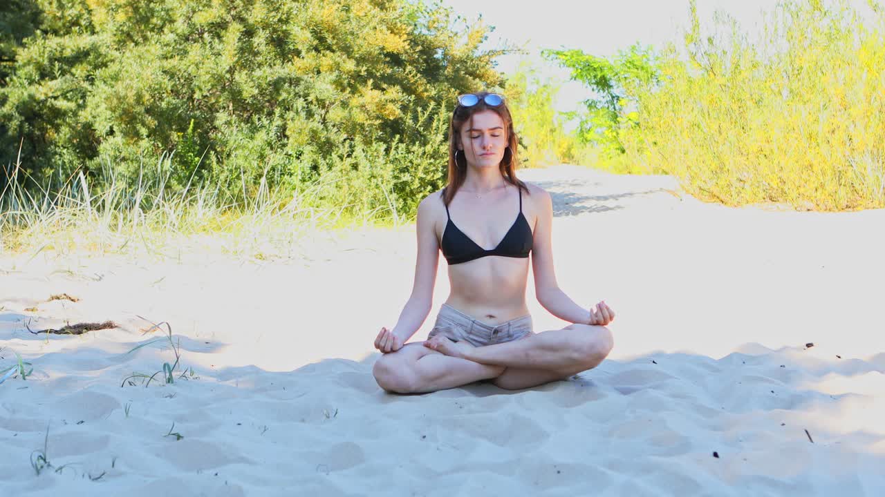 mujer meditando está sentada en posición de loto en la playa de arena en el día de verano