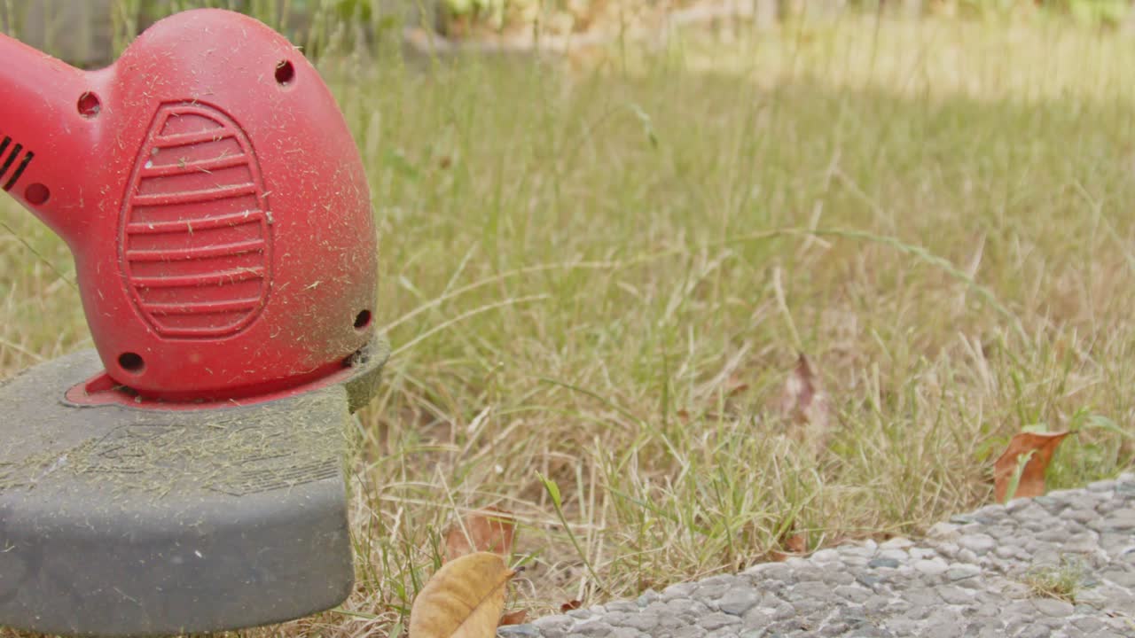 전기 잔디 트림머 는 느린 움직임 으로 정원 잔디 의 높은 잔디 를  ⁇ 는 것