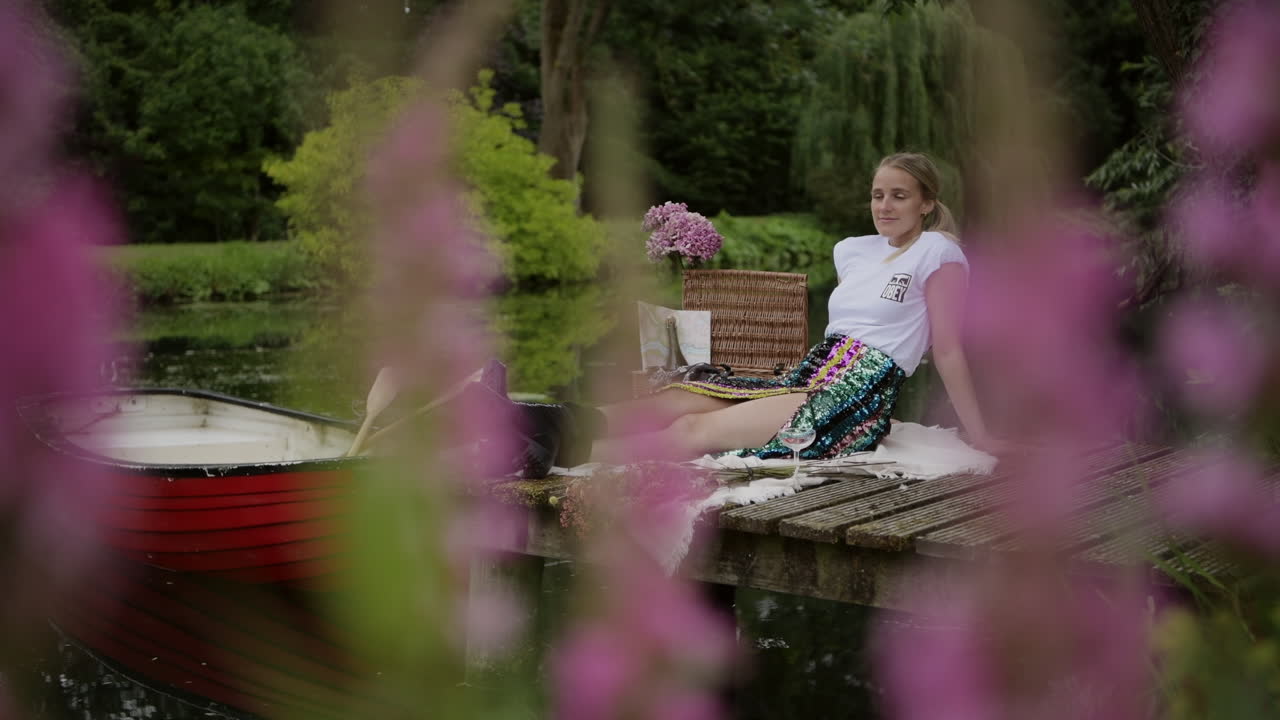 Woman relaxes on wooden jetty at botanical garden with pink flower in foreground