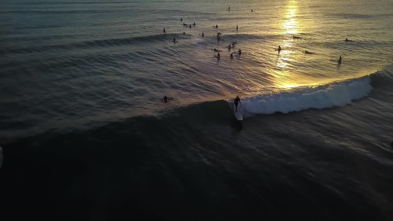 Surfista che cavalca un'onda nel riflesso di un tramonto dorato, riprese aeree con movimento all'indietro.