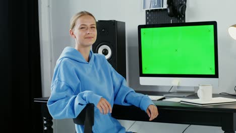joven sonriendo mirando a la cámara sentada frente a un monitor verde