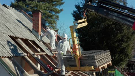 workers dismantling a roof with the help of a crane.