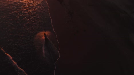 vista panorámica de una mujer montando una motocicleta hacia la puesta de sol en la playa, montando en el agua en la playa de pasut, bali indonesia