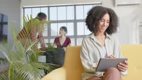 Portrait-of-happy-diverse-casual-businesswoman-using-tablet-sitting-on-sofa-in-office,-slow-motion