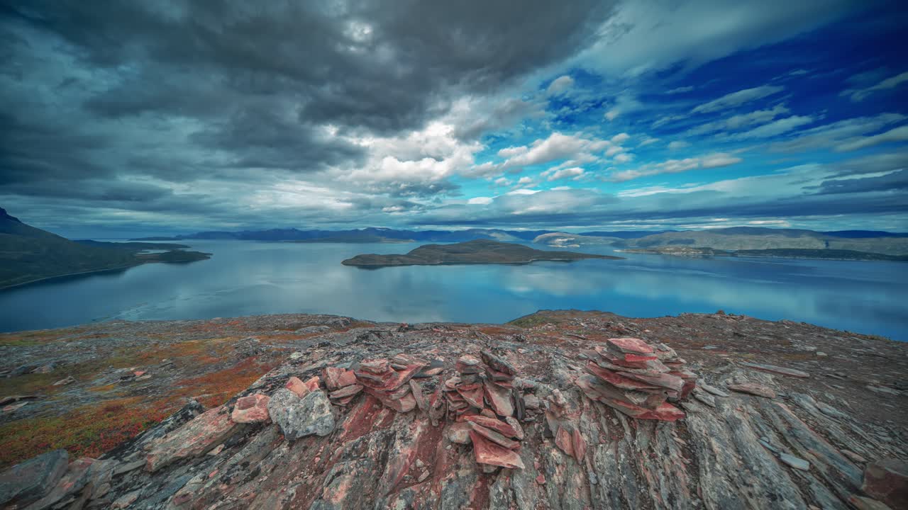 las nubes tormentosas giratorias están iluminadas por el sol poniéndose sobre el sereno fiordo y las montañas marchitadas en el video de lapso de tiempo
