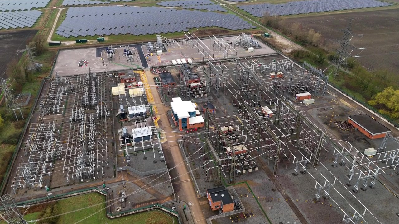 High-angle aerial perspective of a major electrical utility substation and solar field supporting the national grid in Burwell, Cambridgeshire.