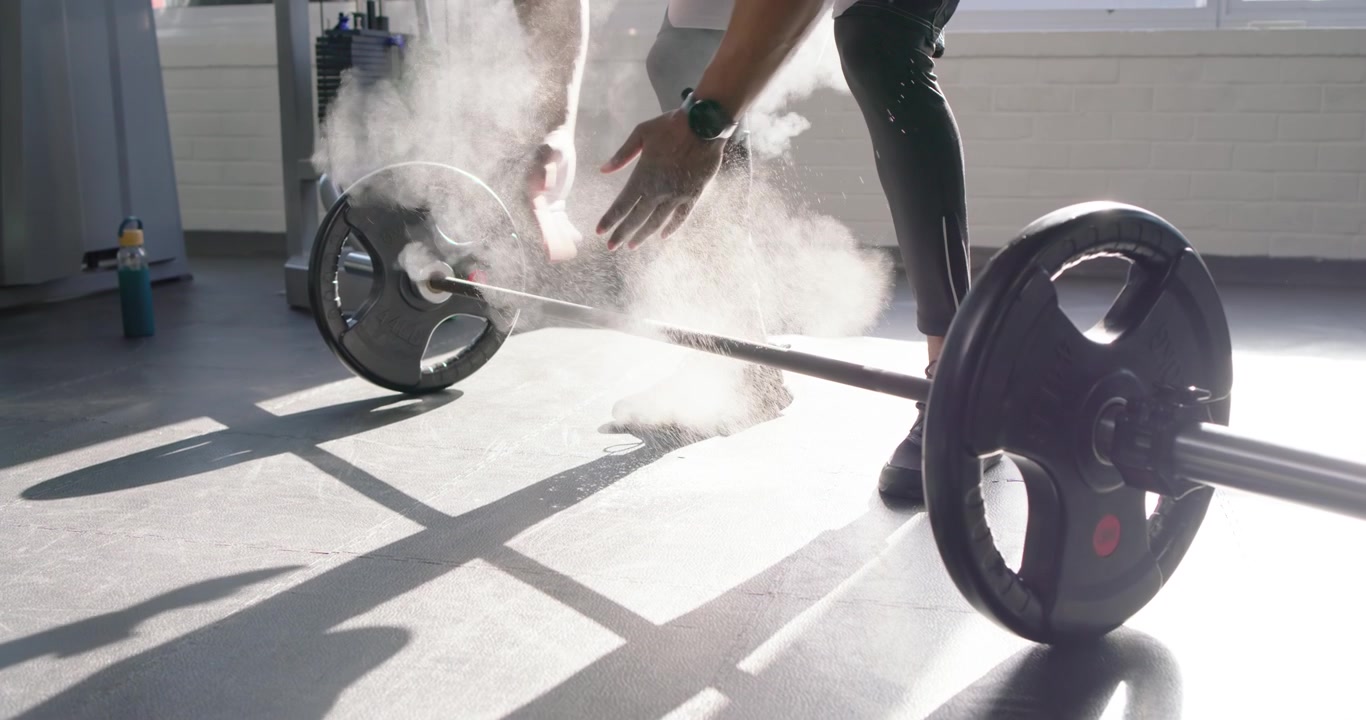African American man at sunlit gym in tank clapping chalk gripping barbell lifting for power