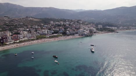 Aerial-of-boats-calmly-resting-on-the-azure-bay-of-Himara,-Albania