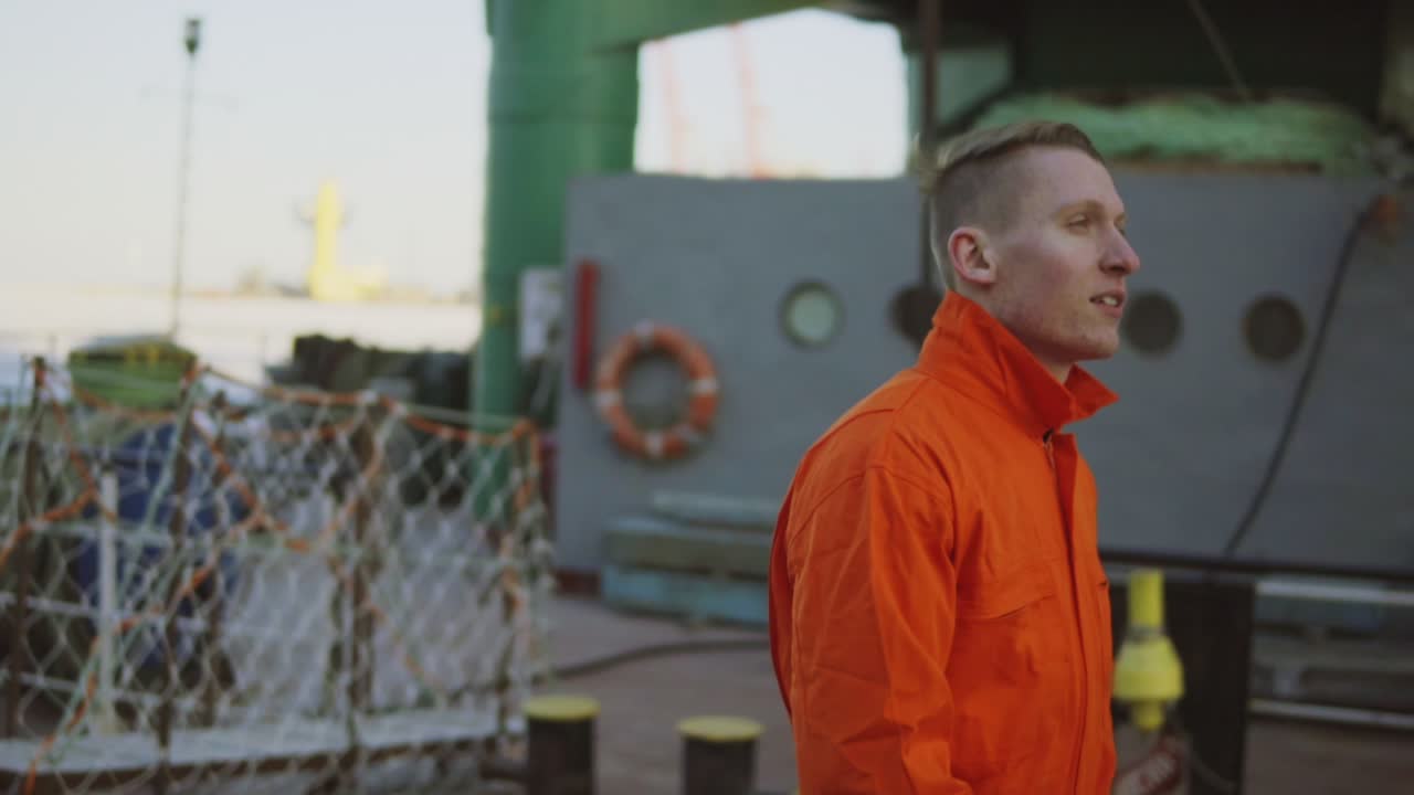 Young worker in orange uniform walking through the harbour by the sea during his break. Leisure time