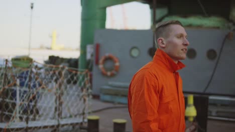 Young-worker-in-orange-uniform-walking-through-the-harbour-by-the-sea-during-his-break.-Leisure-time