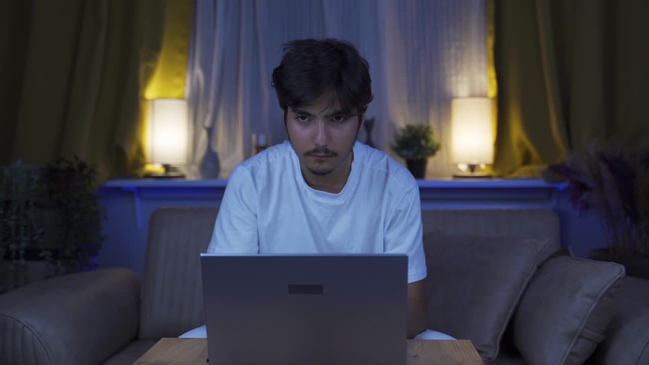 el hombre que se centra en la computadora tiene una expresión seria. en casa por la noche.