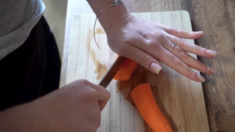 woman cutting carrots with a knife in the kitchen on a wooden cutting board