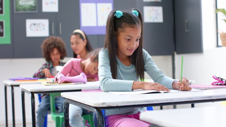 En la escuela, niña escribiendo en cuaderno en el pupitre, concentrada en el trabajo de clase