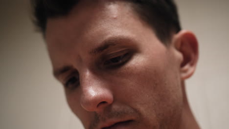 Closeup-of-face-of-unhappy,-sad,-angry,-depressed-attractive,-handsome-man,-criminal-prisoner,-inmate-in-orange-jumpsuit-sitting-in-prison-cell